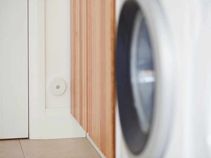 Close-up view of a washing machine in a modern laundry room, featuring a sensor on the wall