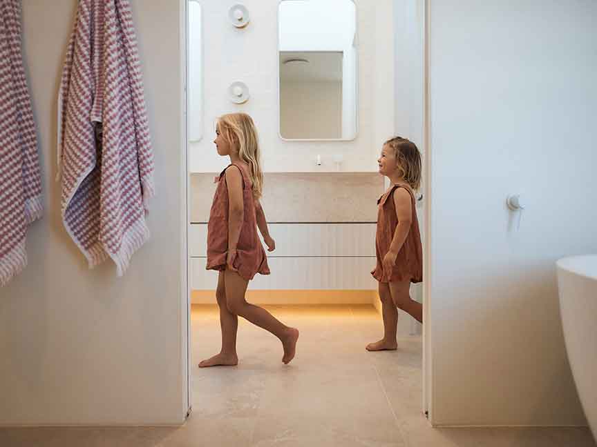 Two siblings, one older and one younger, are walking side by side with the younger one following closely behind the older one