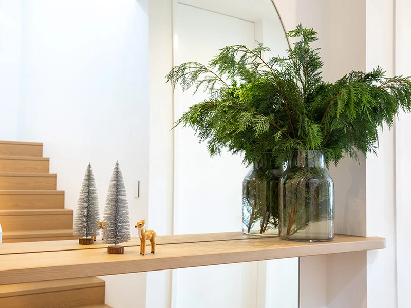 Wooden shelf displays a mirror and a vase filled with lush evergreen plants