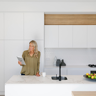 Woman holding an iPad in the kitchen with a white cup on the countertop next to her