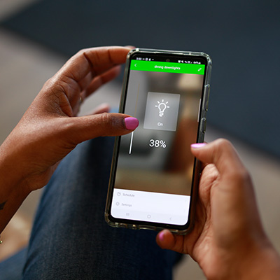 Woman adjusts lights with Wiser by SE app on smartphone