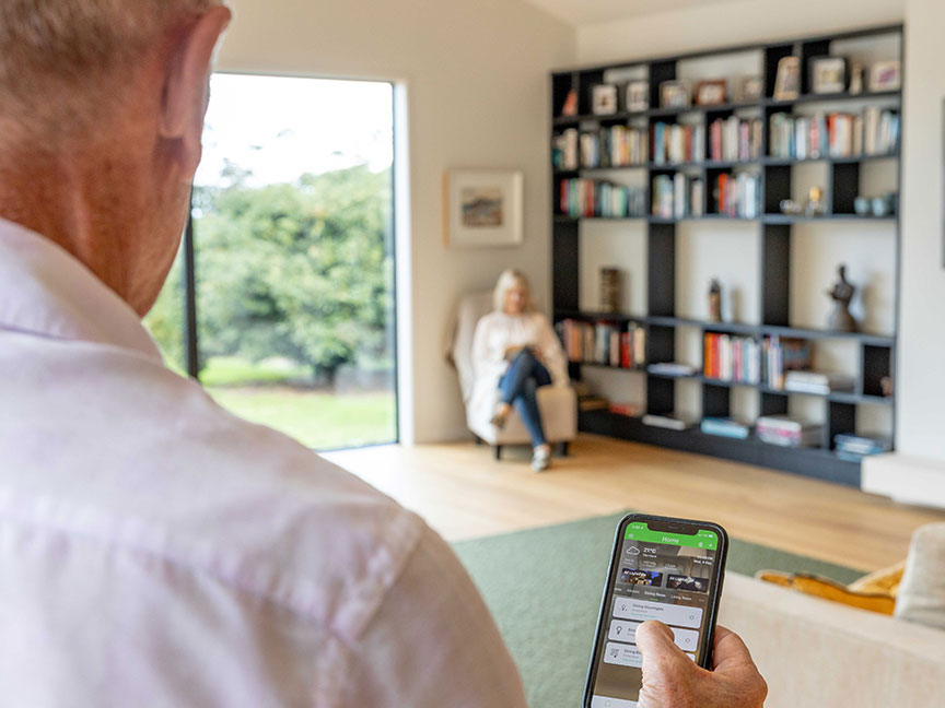 A man holding a smartphone in a living room, engrossed in its screen, surrounded by cozy furniture.