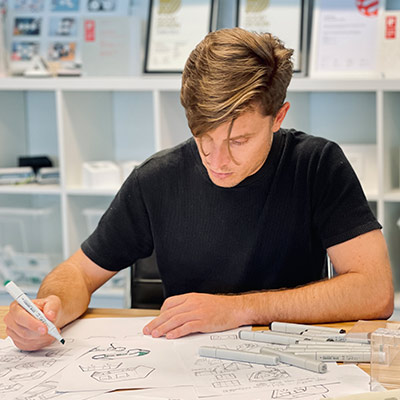 Man seated at a table using a marker to draft a drawing plan on a white paper