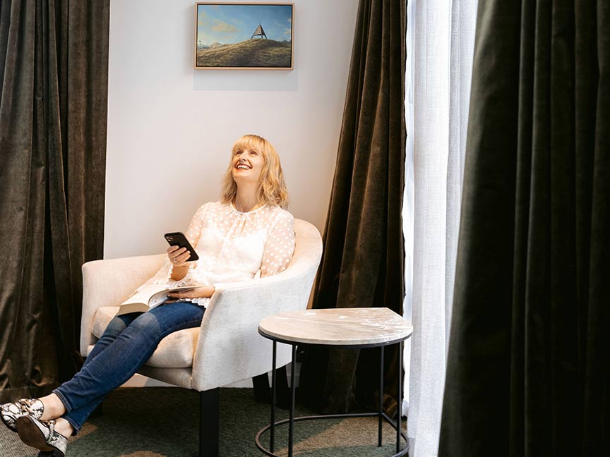 A joyful adult woman lounges on the couch while holding a smartphone