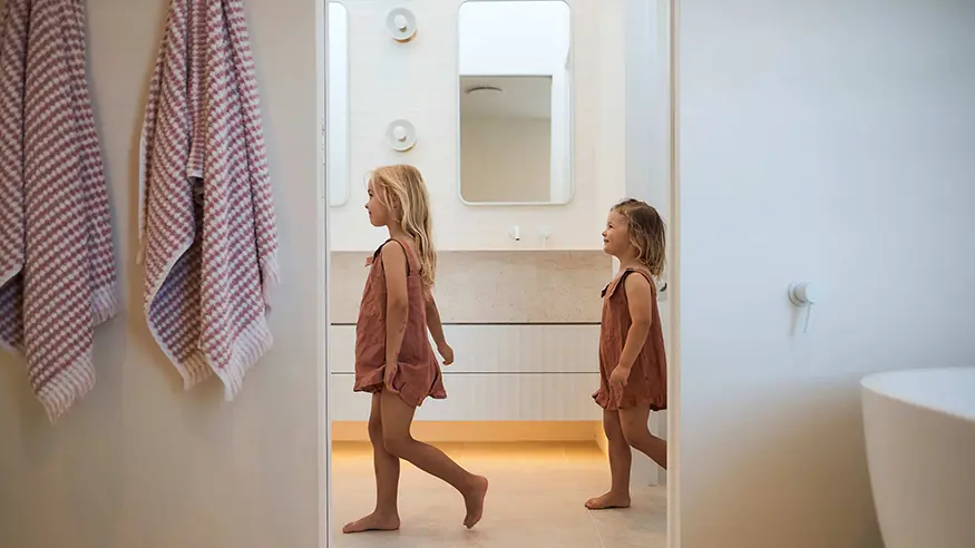 Two children walking in a bathroom.