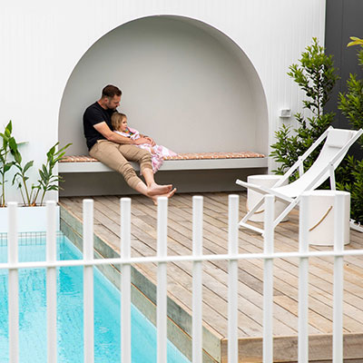 Father and child sitting on a bench by a pool.