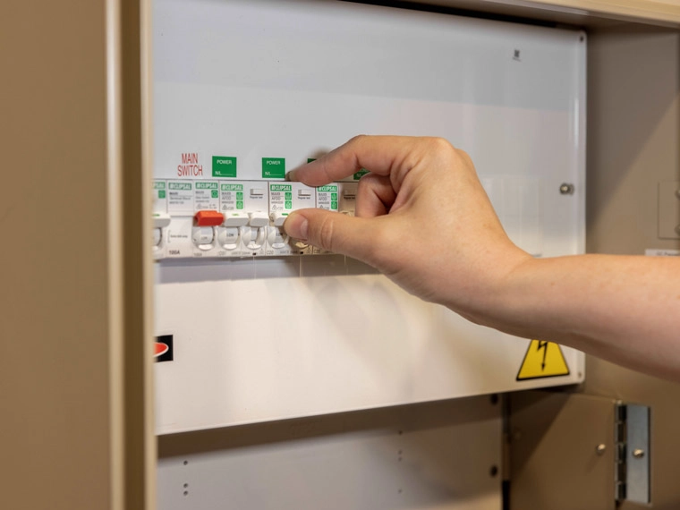 Person operating an industrial power distribution board, switching a circuit breaker in a safety-panel, with focus on the hand and switches.