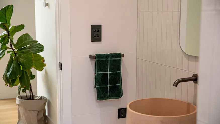 White bathroom wall with light switch and green towel.