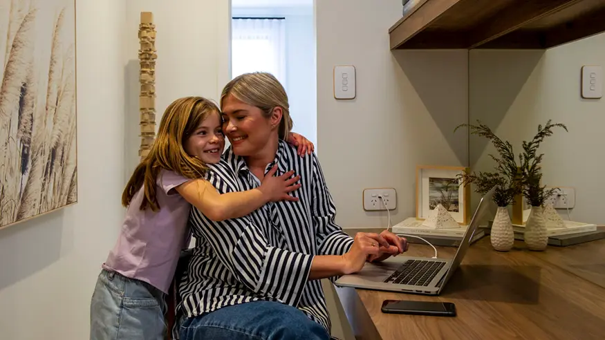 An adult female and a young child sitting at a desk, interacting in a home setting.