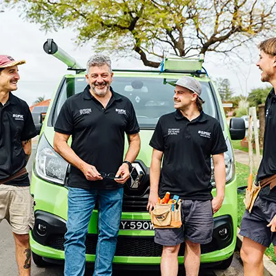 Four Clipsal Electricians in black shirts stand beside a green van.