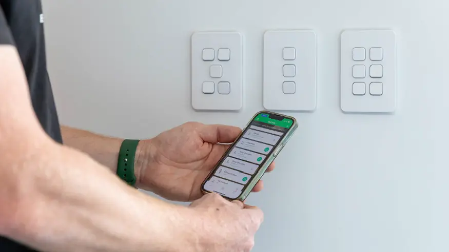 A man using a smart phone to remotely turn on a light switch.