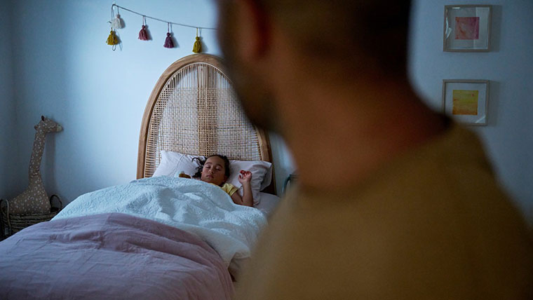 Dad watches daughter sleep peacefully in bed