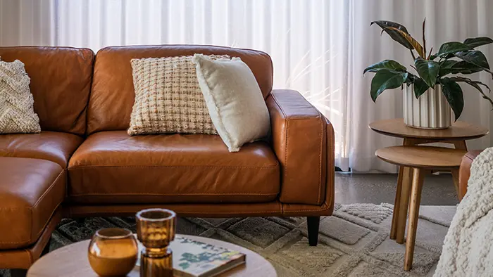 A modern living room features a brown leather sofa with textured cushions, a wooden coffee table, and a plant on a side table.