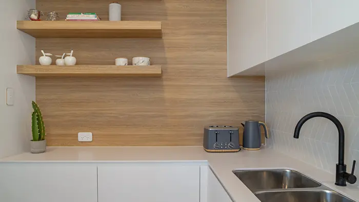 Modern kitchen with a stainless steel sink, spotted kettle, toaster, and a green plant on a light countertop