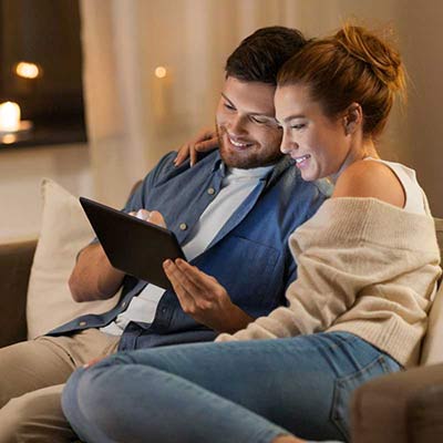 Couple happily using tablet on couch, with husband holding it