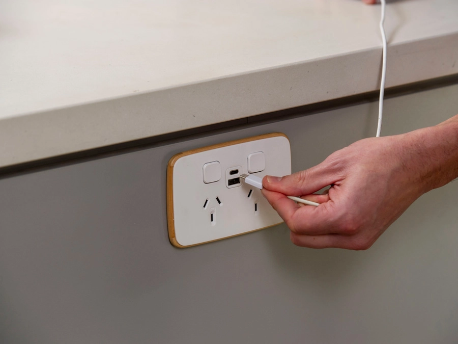 A hand plugging a type-c cable into a wall socket with electrical outlets and USB ports.